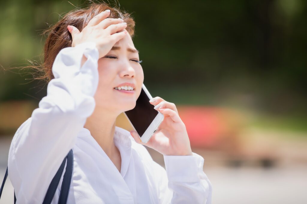 電話で話しながら頭を抱える白いシャツの女性