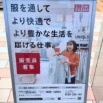 ユニクロ店舗内でシャツを手に取り笑顔で接客する女性スタッフの求人ポスター