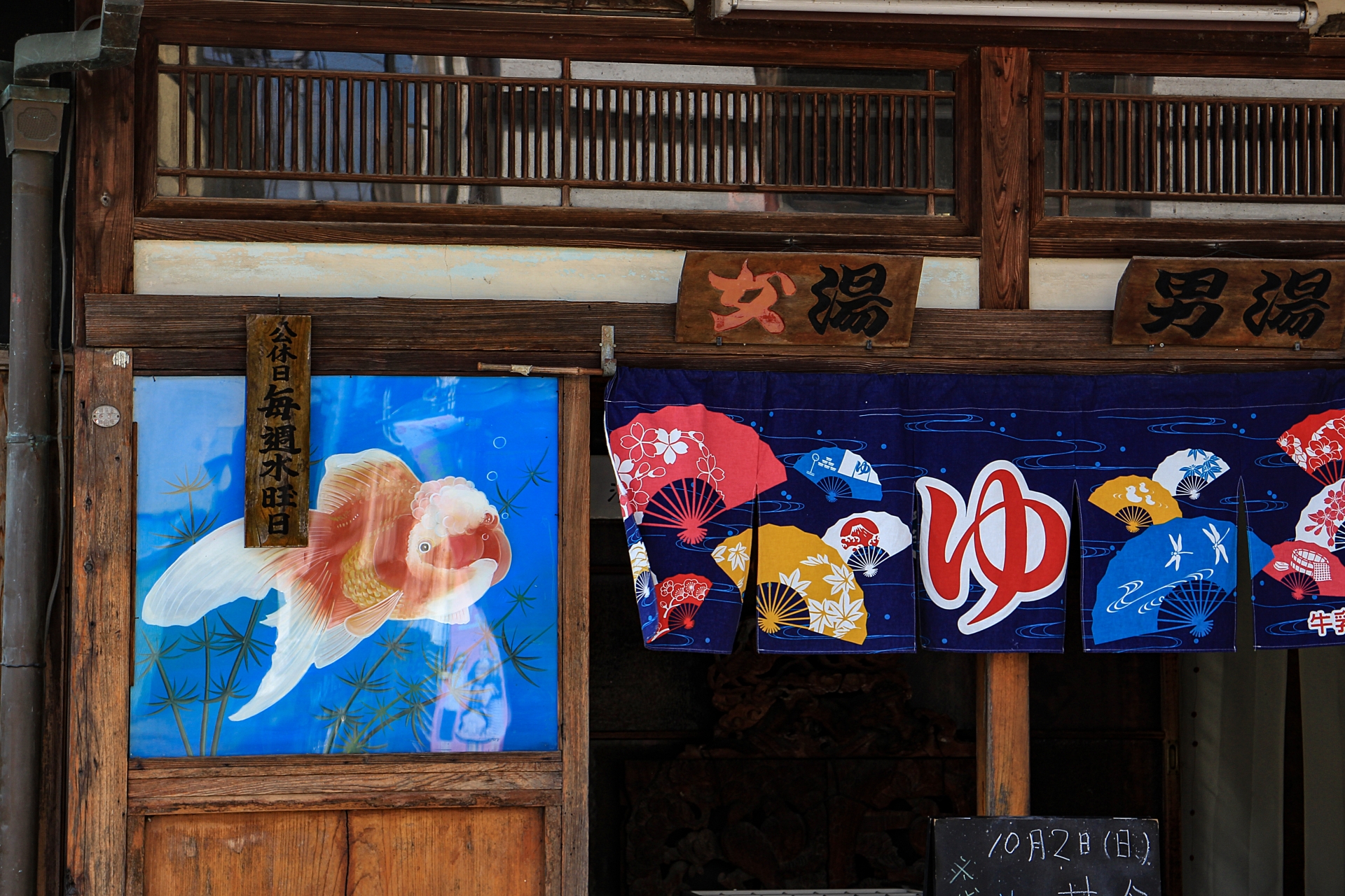 昔ながらの木造建築の銭湯入り口に掛かる男湯・女湯の暖簾と金魚の装飾幕