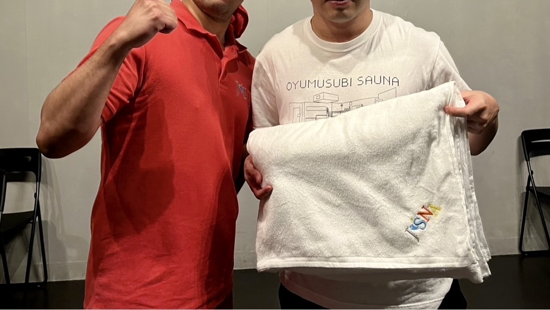 熱波師検定の受講後にJSNAロゴ入りタオルを持つ参加者と講師