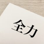 「全力」の文字が印刷された白い紙が木目調のテーブルに置かれている