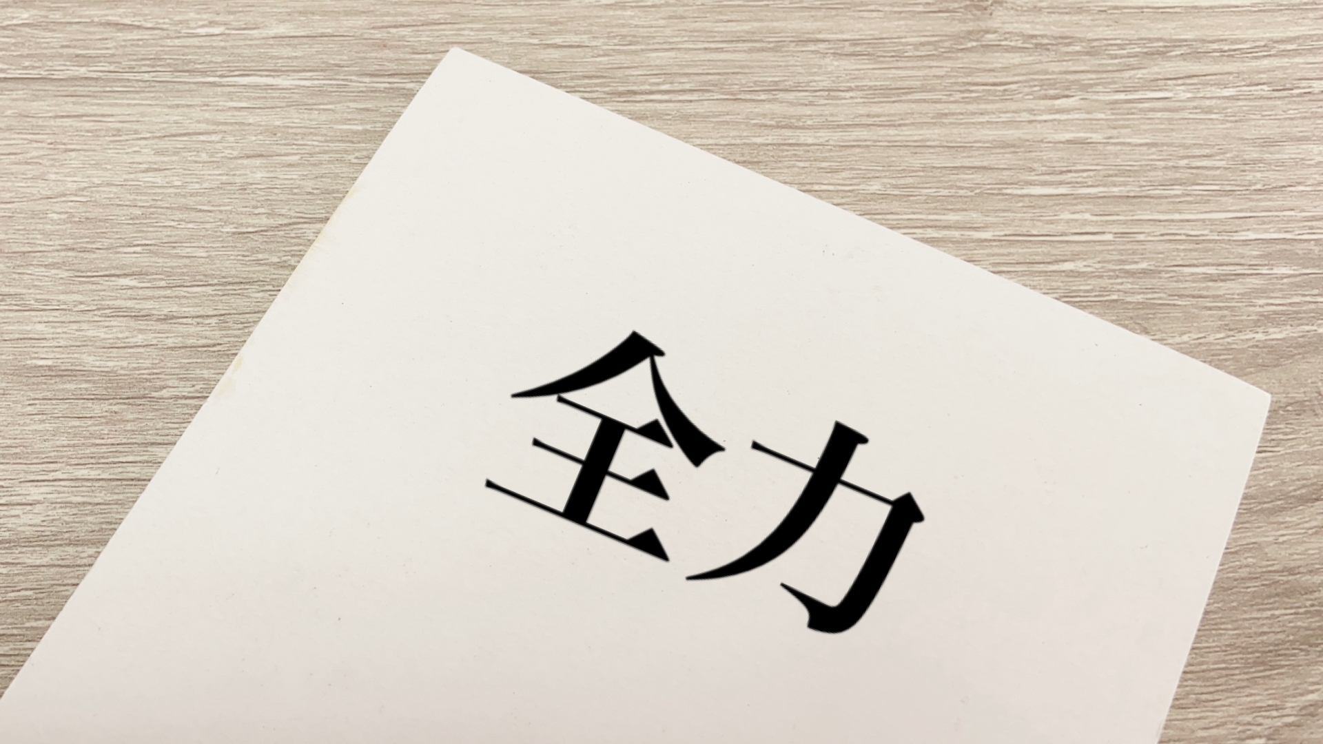「全力」の文字が印刷された白い紙が木目調のテーブルに置かれている
