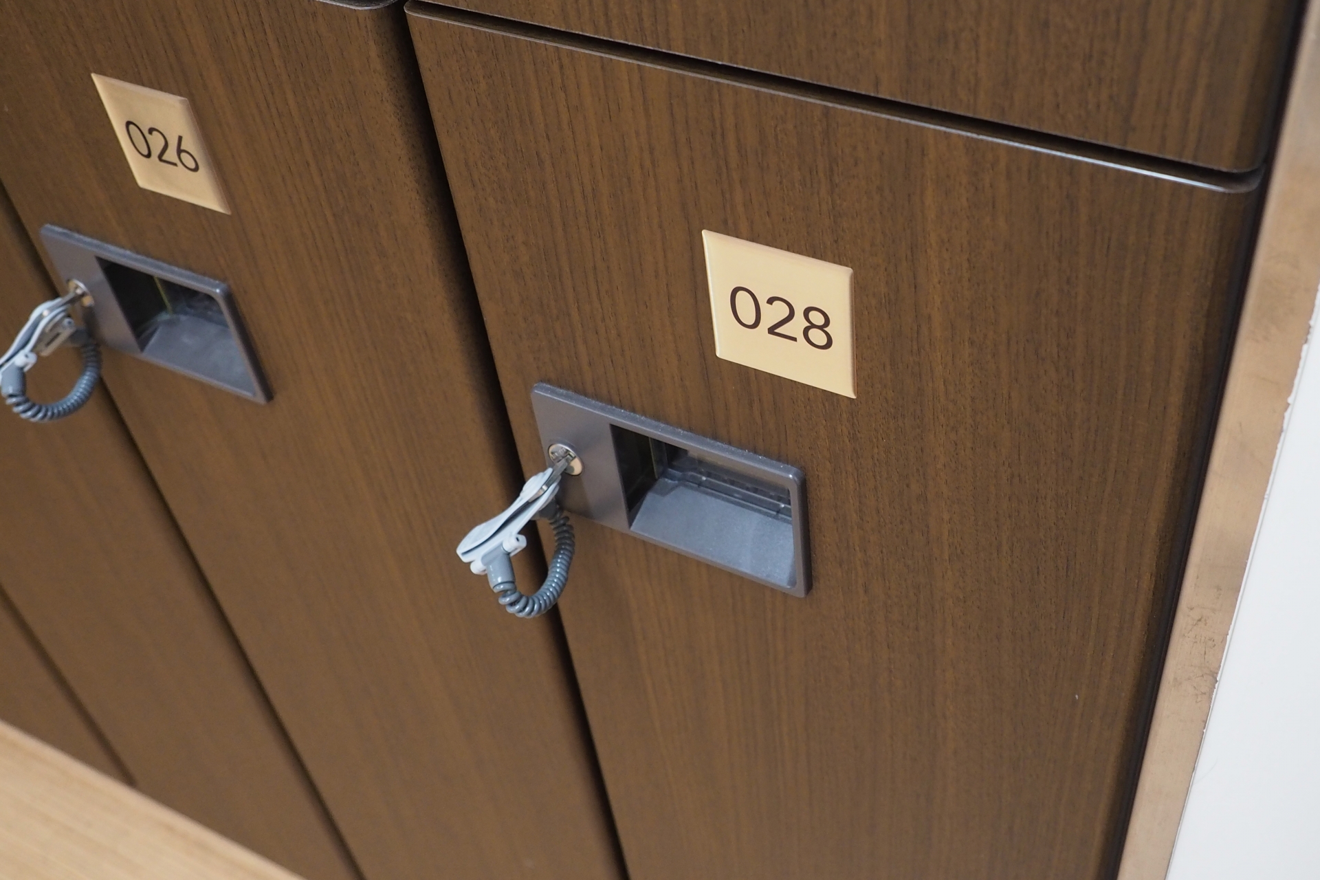 木製ロッカーの一部と鍵付きのロック機構、番号「028」が表示されている