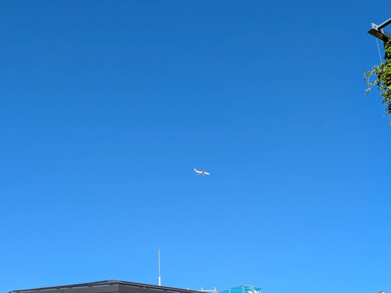 快晴の青空を飛行する旅客機と屋上のアンテナが見える建物