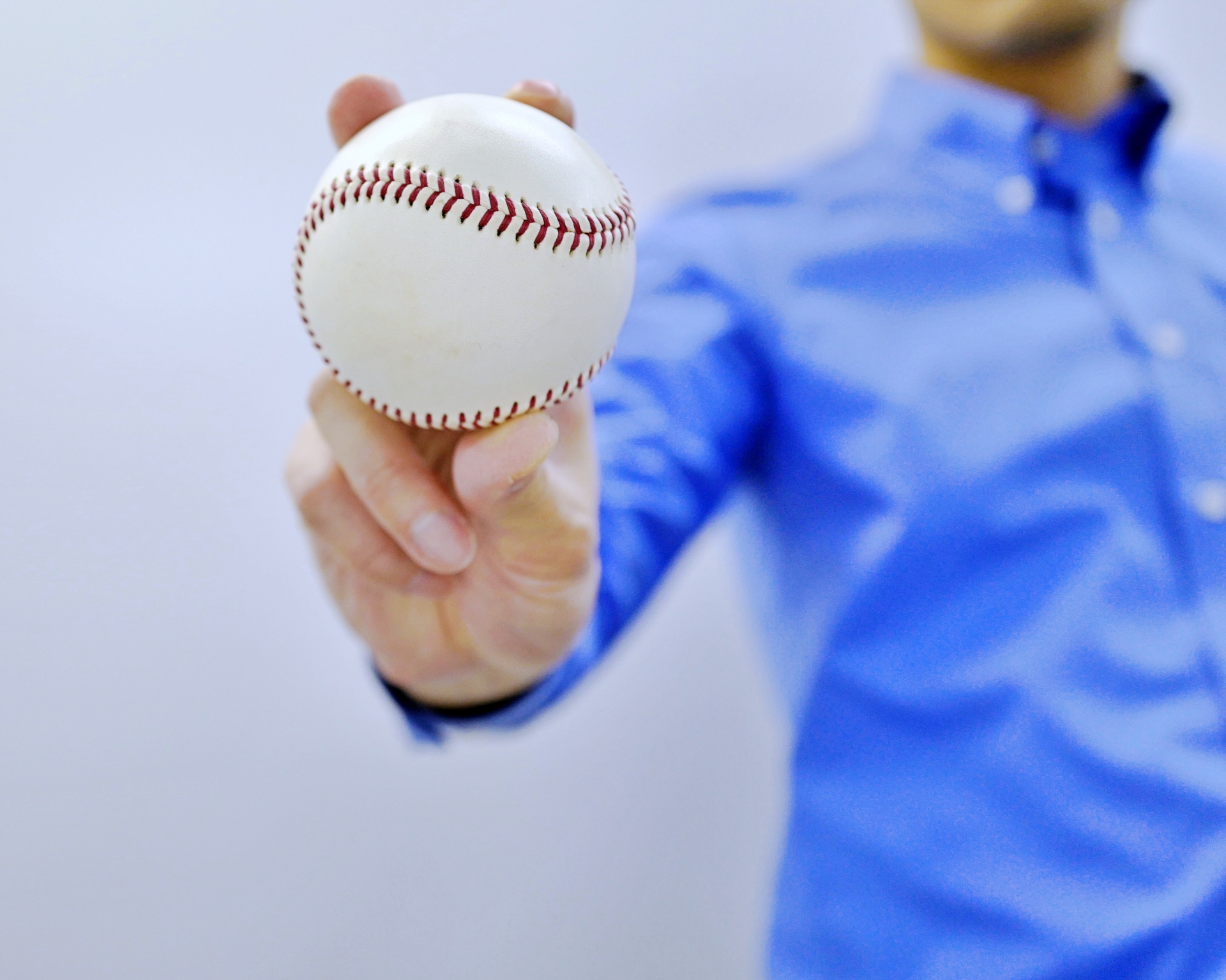 青いシャツを着た男性が野球ボールを手に持って前方に差し出している様子