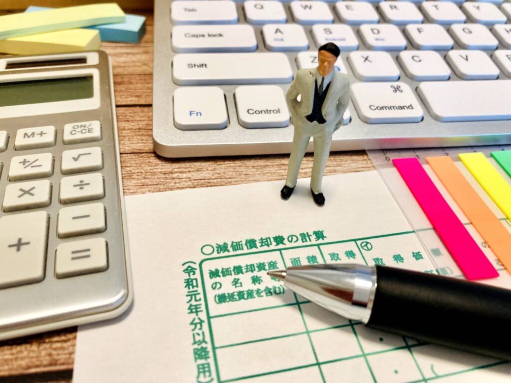 減価償却費の計算用紙と電卓、キーボードに囲まれたビジネスシーンのイメージ