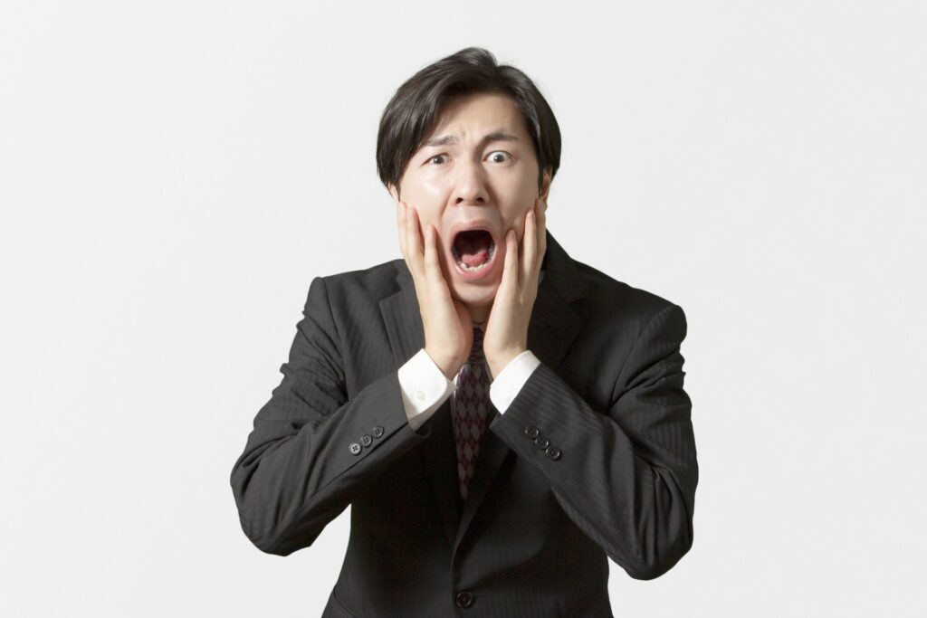 驚いた表情で両手を頬に当てるスーツ姿の男性