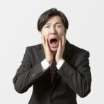 驚いた表情で両手を頬に当てるスーツ姿の男性