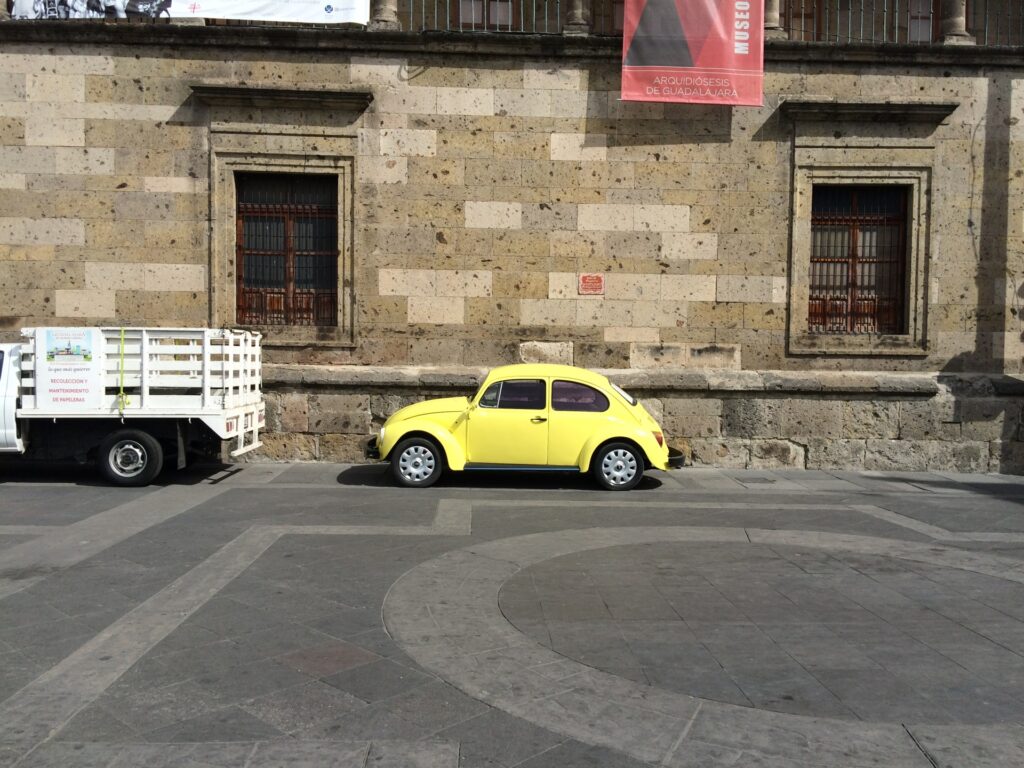 石造りの建物の前に停車している黄色のフォルクスワーゲン・ビートル