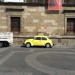 石造りの建物の前に停車している黄色のフォルクスワーゲン・ビートル