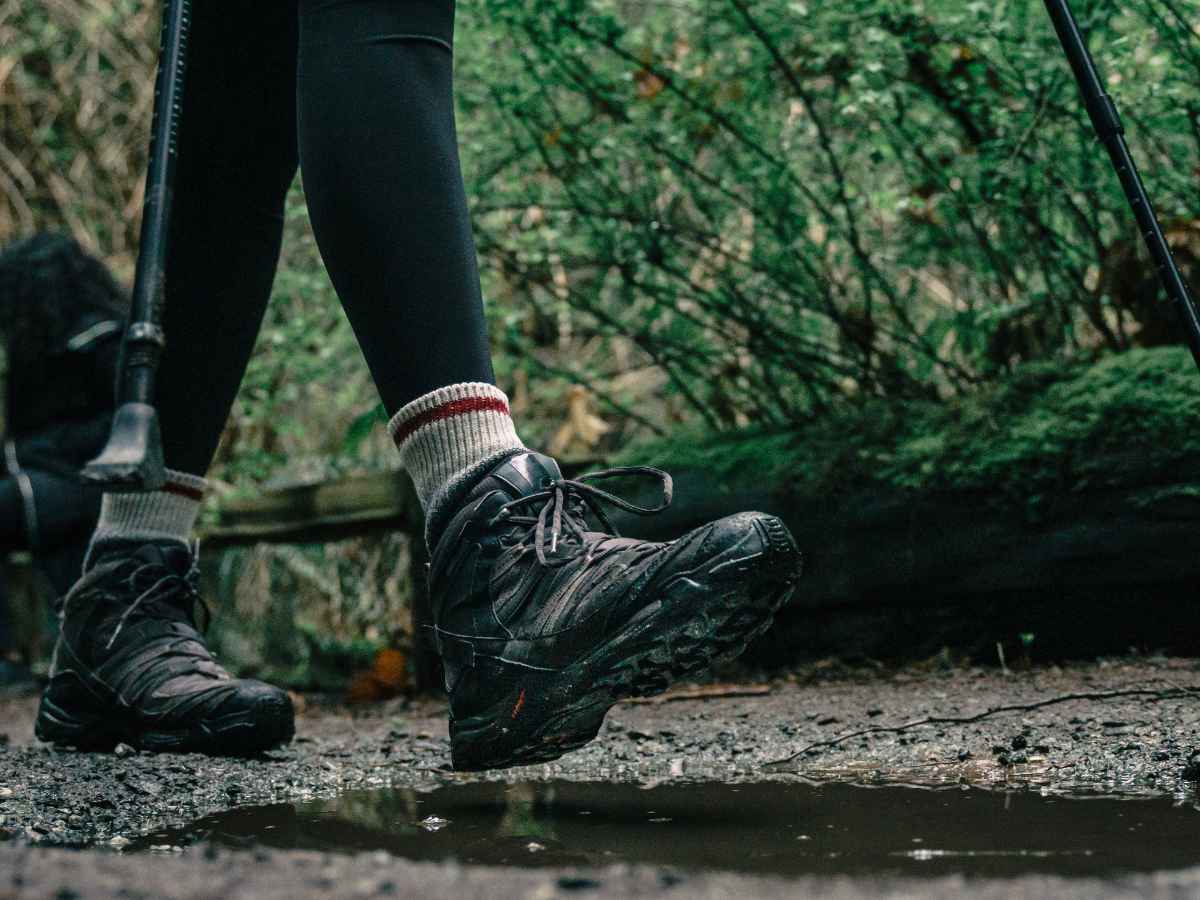 森林の登山道を歩くサロモンのトレッキングシューズを履いた人物の足元