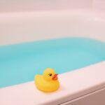 青い湯の張られた浴槽の縁に置かれた黄色いアヒルのおもちゃ