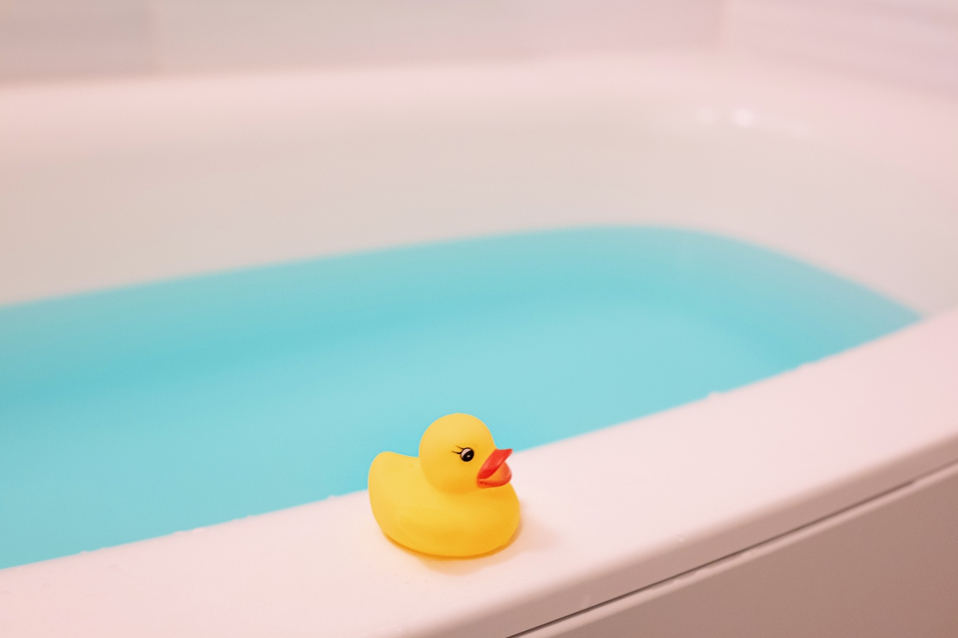 青い湯の張られた浴槽の縁に置かれた黄色いアヒルのおもちゃ