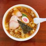 醤油ラーメンの丼にチャーシュー、ナルト、海苔、ネギが添えられた温かい一杯