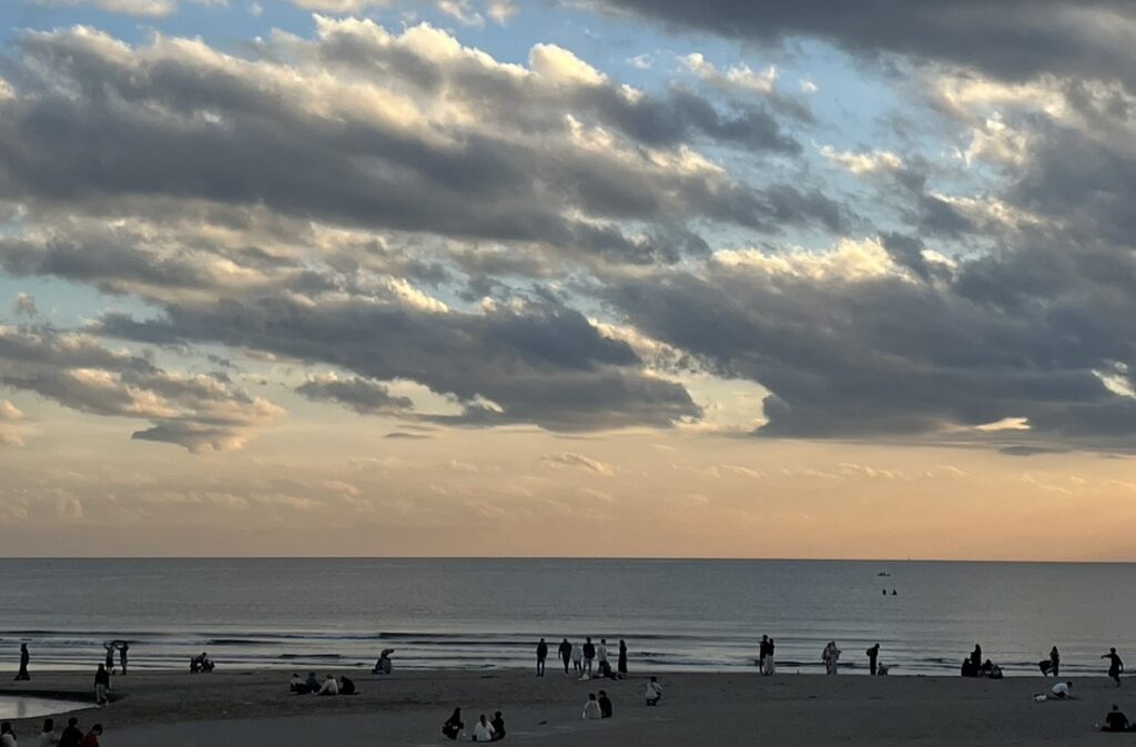 夕暮れの海辺で人々が思い思いに過ごす静かな浜辺の風景