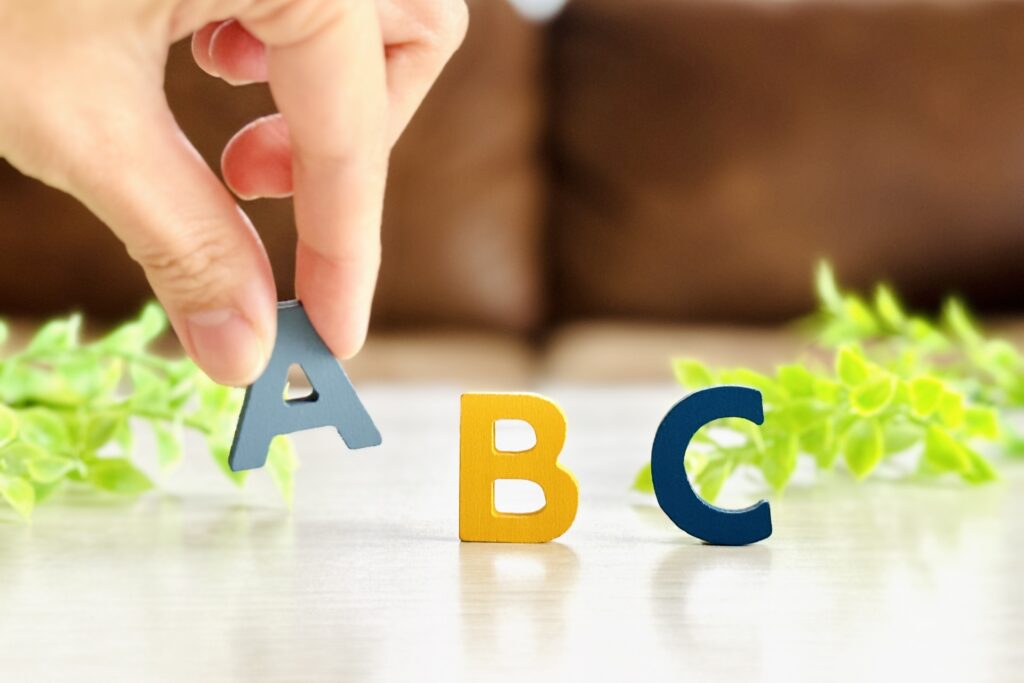 手がアルファベットのAをつまんで並べている様子、ABC分析のイメージ
