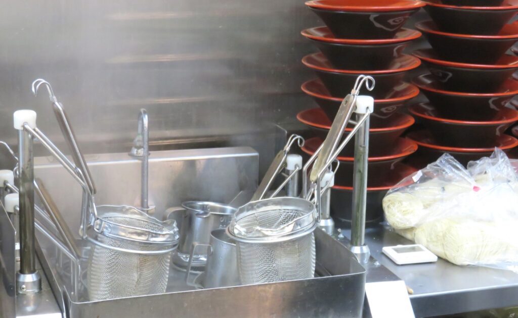 ラーメン店の厨房で麺を茹でるための湯切りざると器が並ぶ様子
