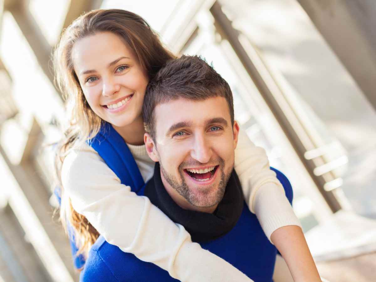 屋内で男性が女性を背負い、二人が笑顔でカメラを見ている様子。