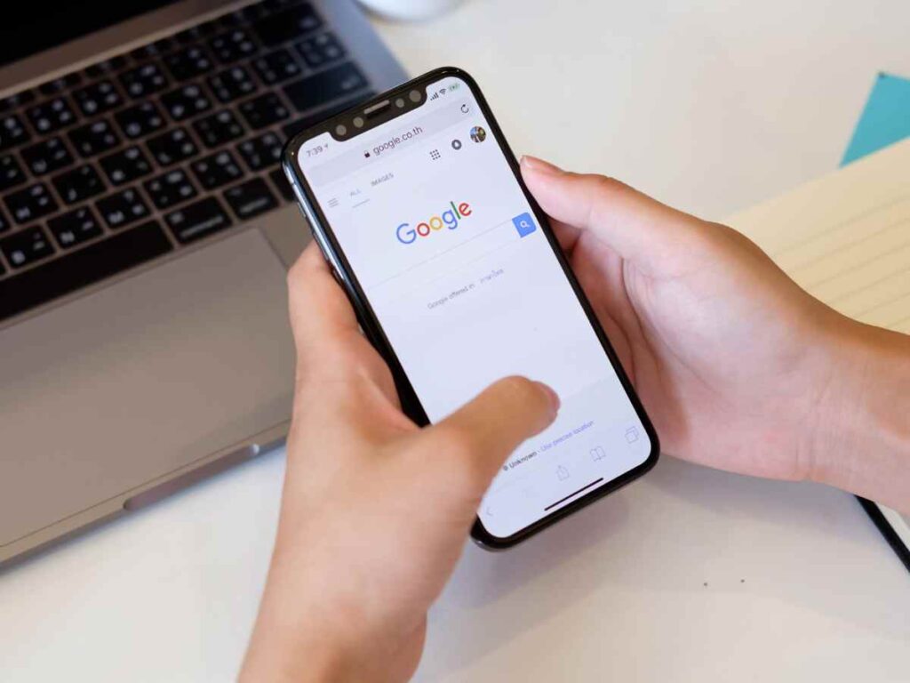 スマートフォンでGoogle検索画面を開く手元とノートPCの作業風景