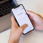 スマートフォンでGoogle検索画面を開く手元とノートPCの作業風景