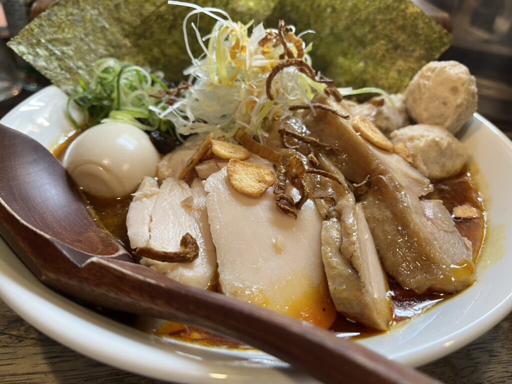 醤油系スープのラーメンにチャーシュー、味玉、海苔、刻みネギが盛り付けられている様子。