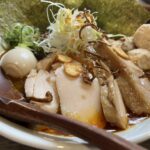 醤油系スープのラーメンにチャーシュー、味玉、海苔、刻みネギが盛り付けられている様子。