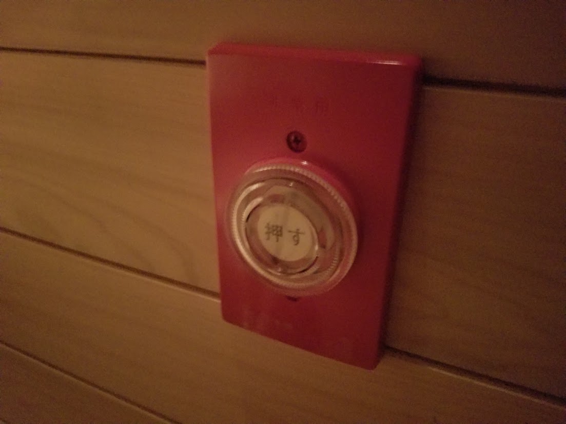 木製パネルの壁面に設置された赤色の非常用押しボタンが写っているサウナ室内の様子。