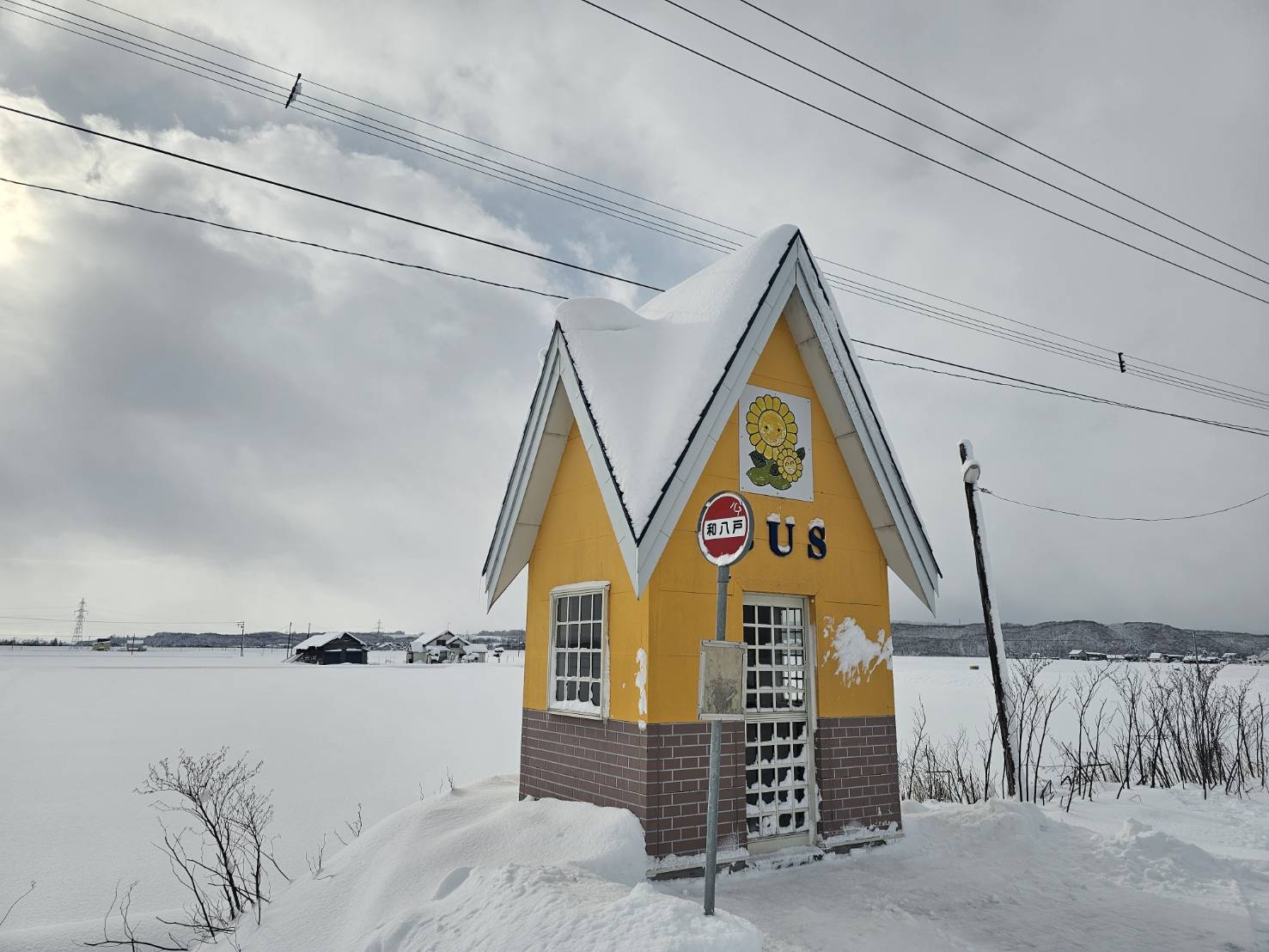 雪原に建つ黄色い小屋型バス停と積雪した屋根の風景