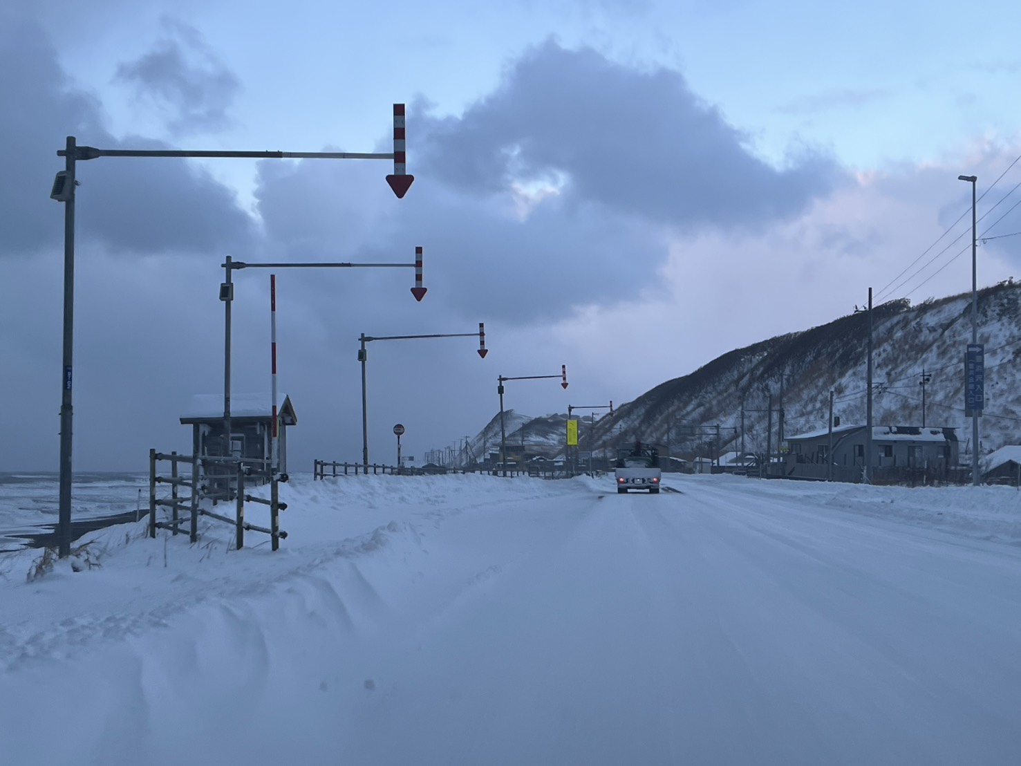 北海道の海沿いを走る雪道でホワイトアウトに近い視界の中を走行する車と雪景色