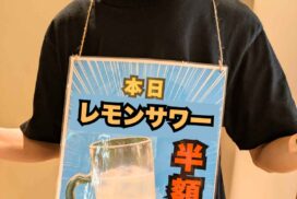 黒いTシャツを着たスタッフが首から「本日 レモンサワー 半額」と書かれたPOPを下げて立っている様子