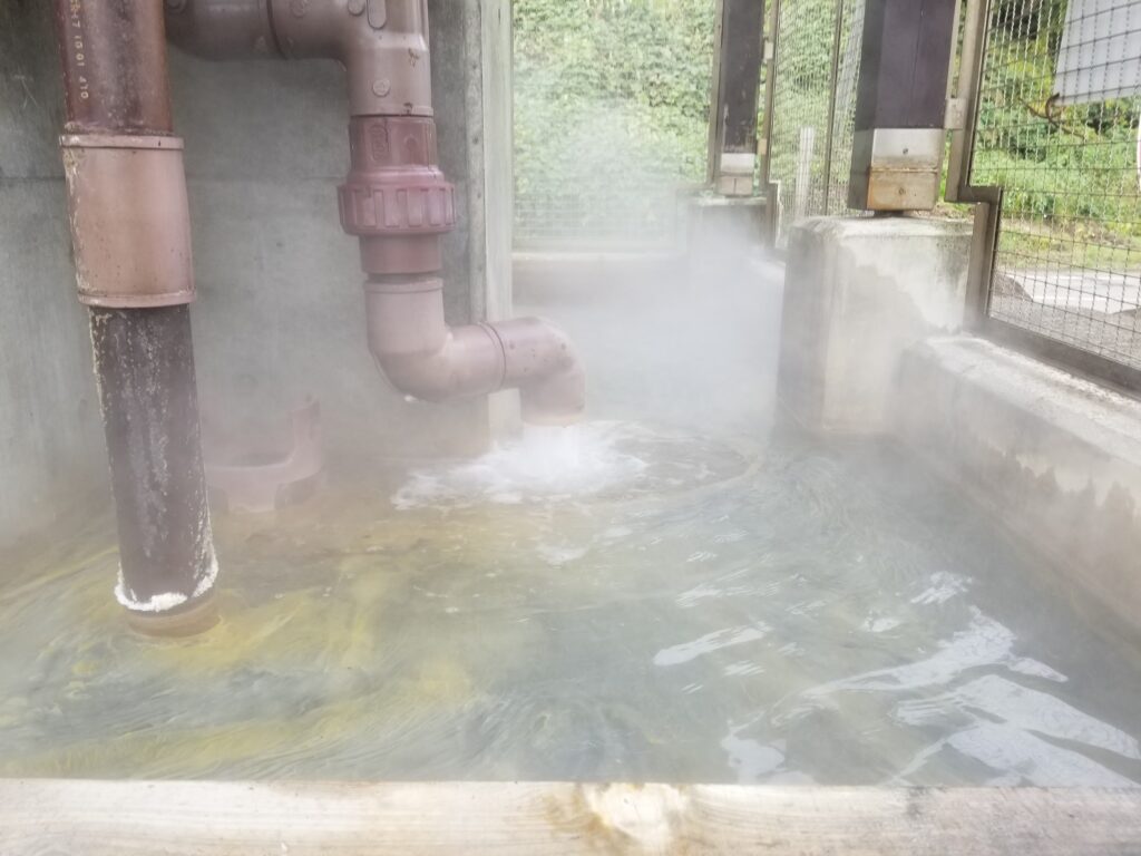 配管から湯が流れ込み蒸気が立ち上る温浴施設の源泉設備の様子。