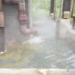 配管から湯が流れ込み蒸気が立ち上る温浴施設の源泉設備の様子。