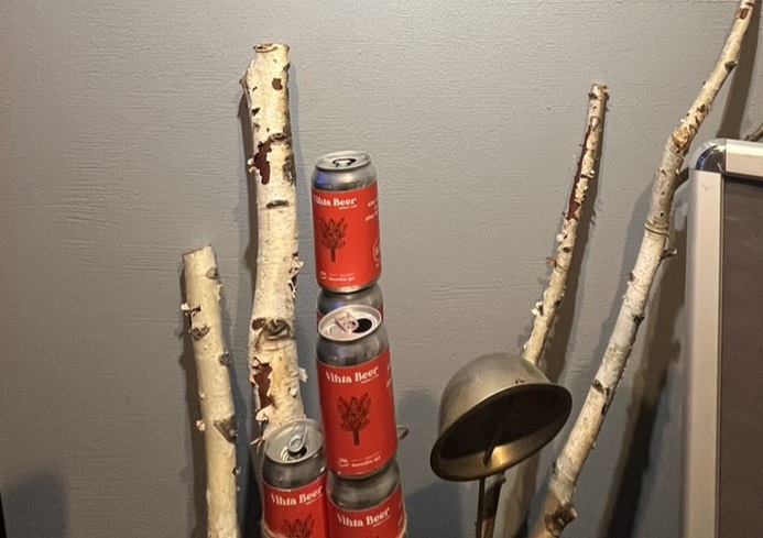 白樺の枝と赤いビール缶が室内の壁際に立てかけて配置されているサウナ装飾の様子。
