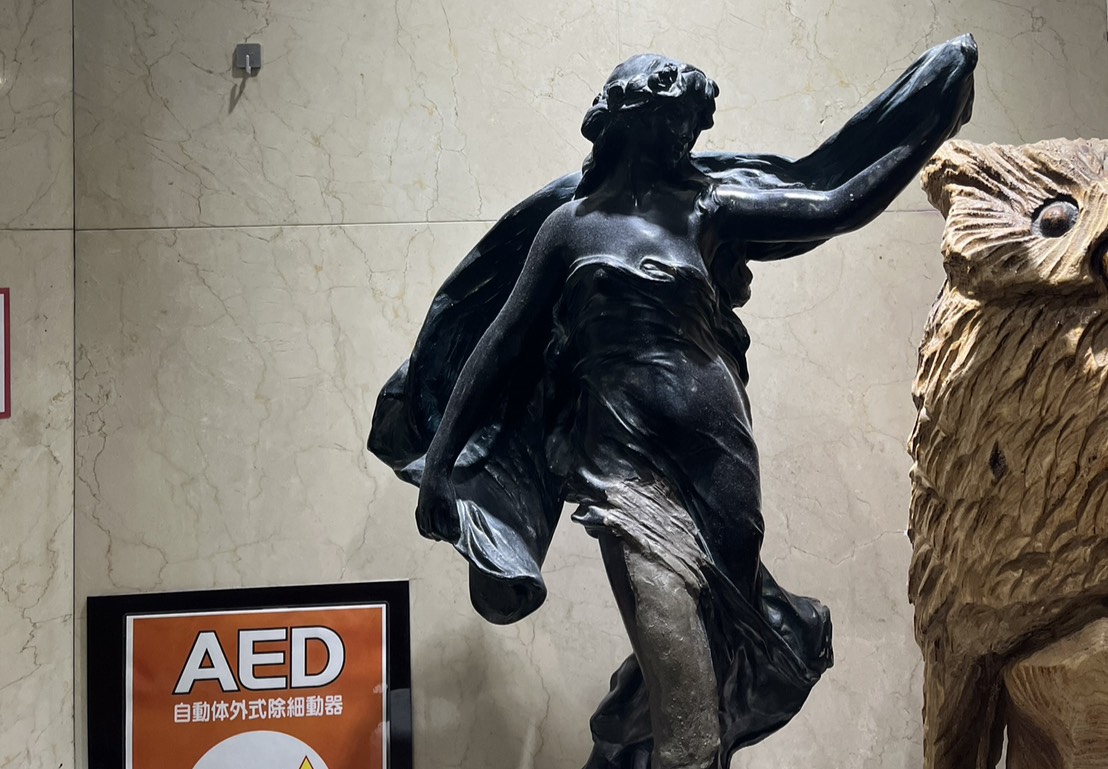 屋内ロビーに設置された女性像の彫刻とAED案内表示が並んでいる様子。
