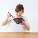 女性がテーブルで丼を持ち、箸で食事をしている様子。
