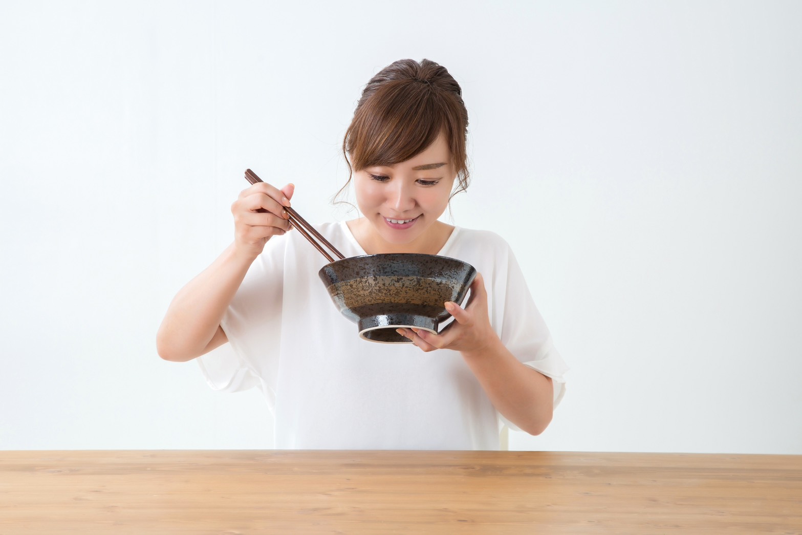 女性がテーブルで丼を持ち、箸で食事をしている様子。