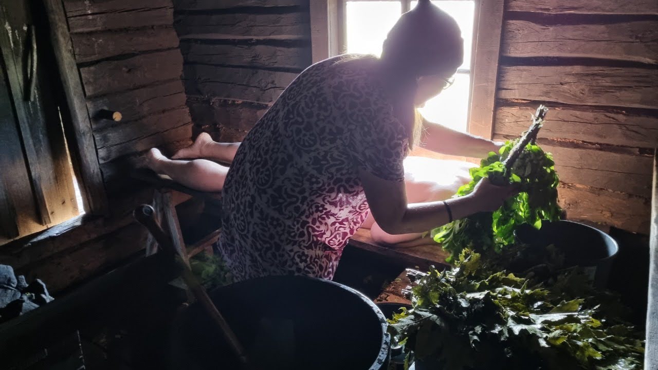 木造サウナ室で利用者に対して白樺の枝葉を使ったウィスキングを行っている施術風景。