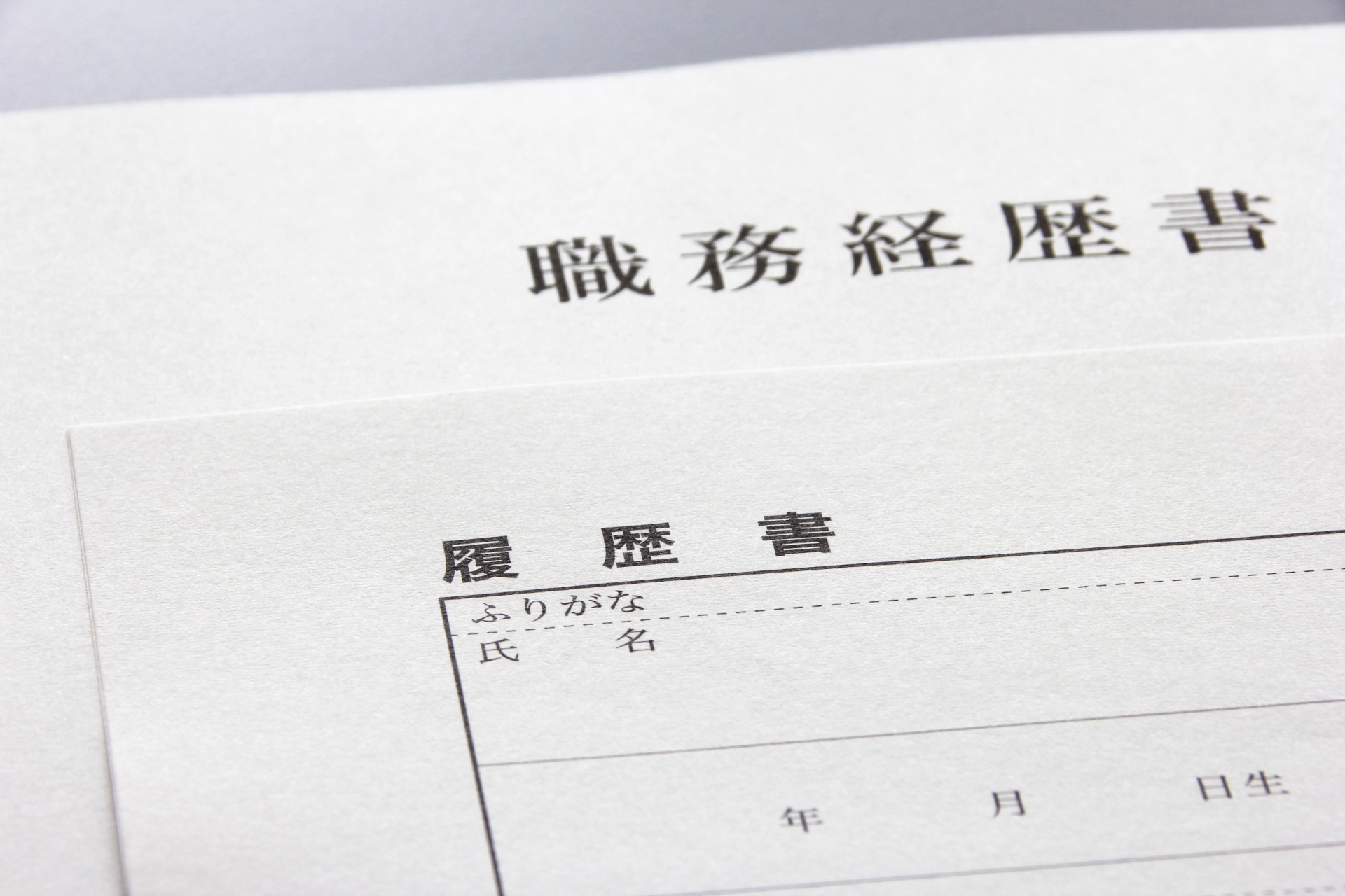 白い背景の上に温浴施設の求人応募などで使用される職務経歴書と履歴書の用紙が重ねて置かれています。