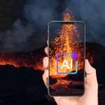 噴火する火山の背景の前に、画面にAIという文字が浮かび上がっているスマートフォンを持つ手が写っています。