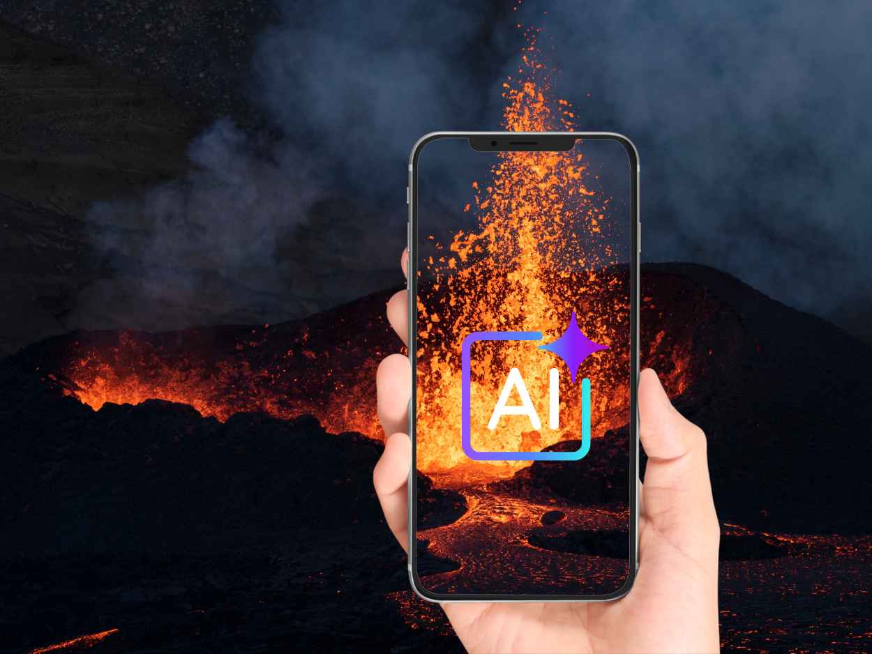 噴火する火山の背景の前に、画面にAIという文字が浮かび上がっているスマートフォンを持つ手が写っています。