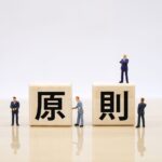白い背景に「原則」と書かれた2つの木製ブロックが置かれ、その周囲や上にスーツ姿の小さなミニチュア人形が配置されています。