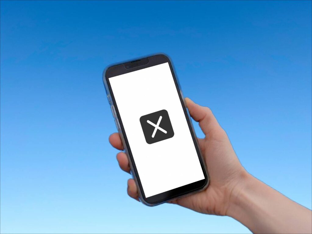 青空を背景にして、画面の中央に大きくバツ印が記されたスマートフォンを手に持っています。
