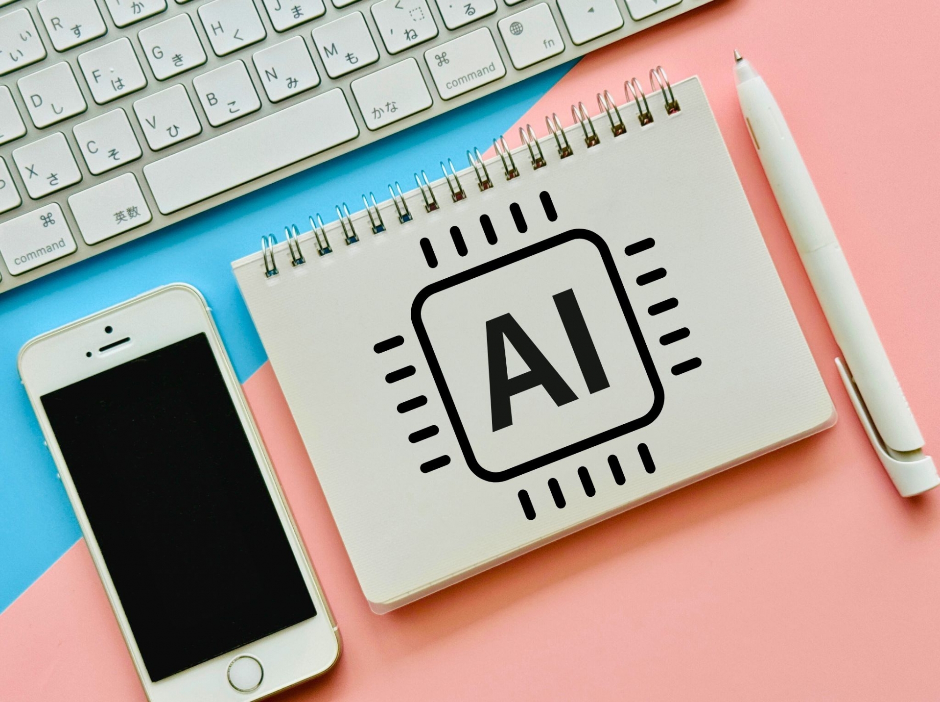 ノートに描かれたAIチップのイラストとキーボード、スマートフォン、ペンが机の上に並んでいるAIイメージ写真です。