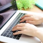 明るい木目調のデスクで、ノートパソコンのキーボードを両手で操作している様子