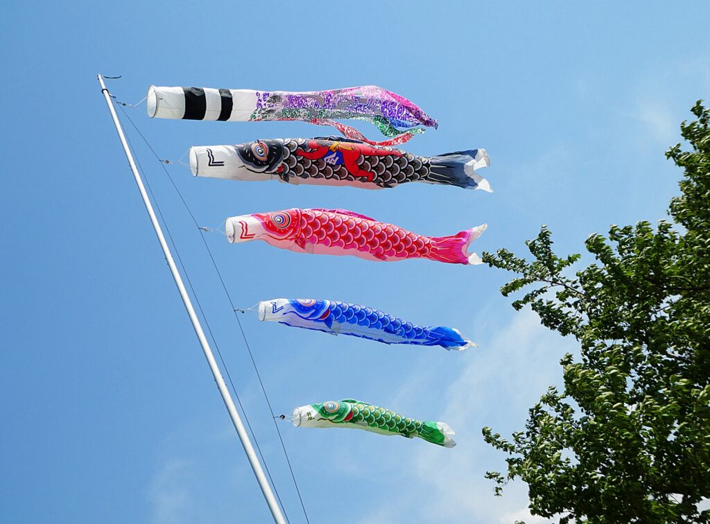 青空を背景に、五色の吹き流しと四匹の鯉のぼりが風にたなびいています。