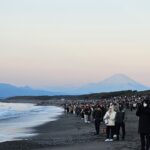 冬の海岸で富士山を背景に日の出を待つ大勢の人々の様子