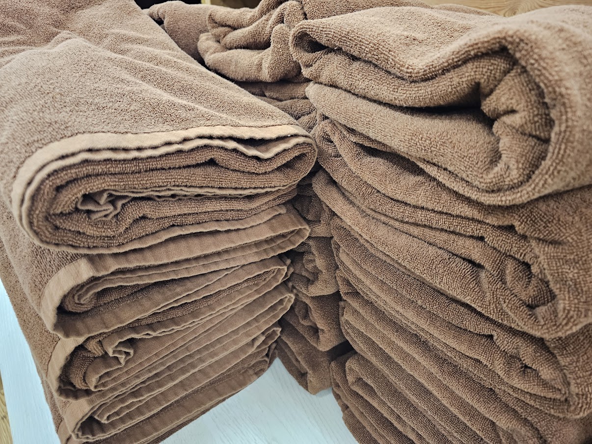 温浴施設の備品棚に、茶色のフェイスタオルが整然と高く積み上げられています