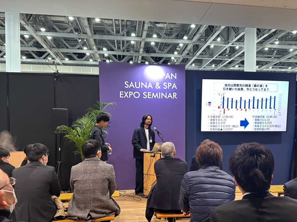 温浴施設の運営者がイベント会場で講演を行っている様子です