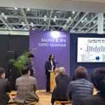 温浴施設の運営者がイベント会場で講演を行っている様子です