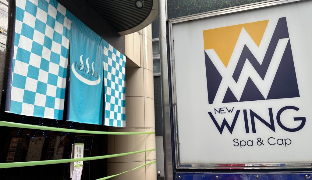 サウナ施設ニューウイングの入り口にある青と白の市松模様ののぼりとロゴ看板。